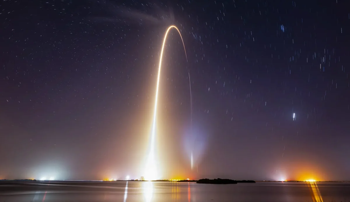 Long-exposure photo of a rocket launch lighting up the night sky with a curved trail
