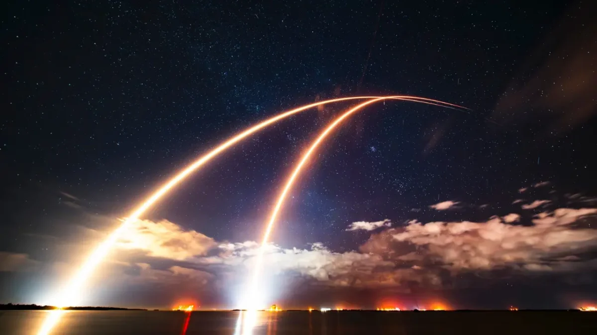 Long-exposure photo of SpaceX Falcon 9 Starlink 6-89 launch creating bright rocket trails across a starry night sky at Kennedy Space Center, Florida.