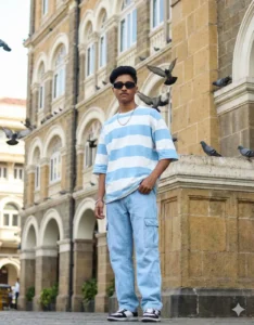 Young boy posing in a blue striped oversized T-shirt and cargo jeans at Grand Hotel Mumbai with flying pigeons – styled for 5 Gemini AI Photo Editing Prompts for Boys 2025. Scipuz