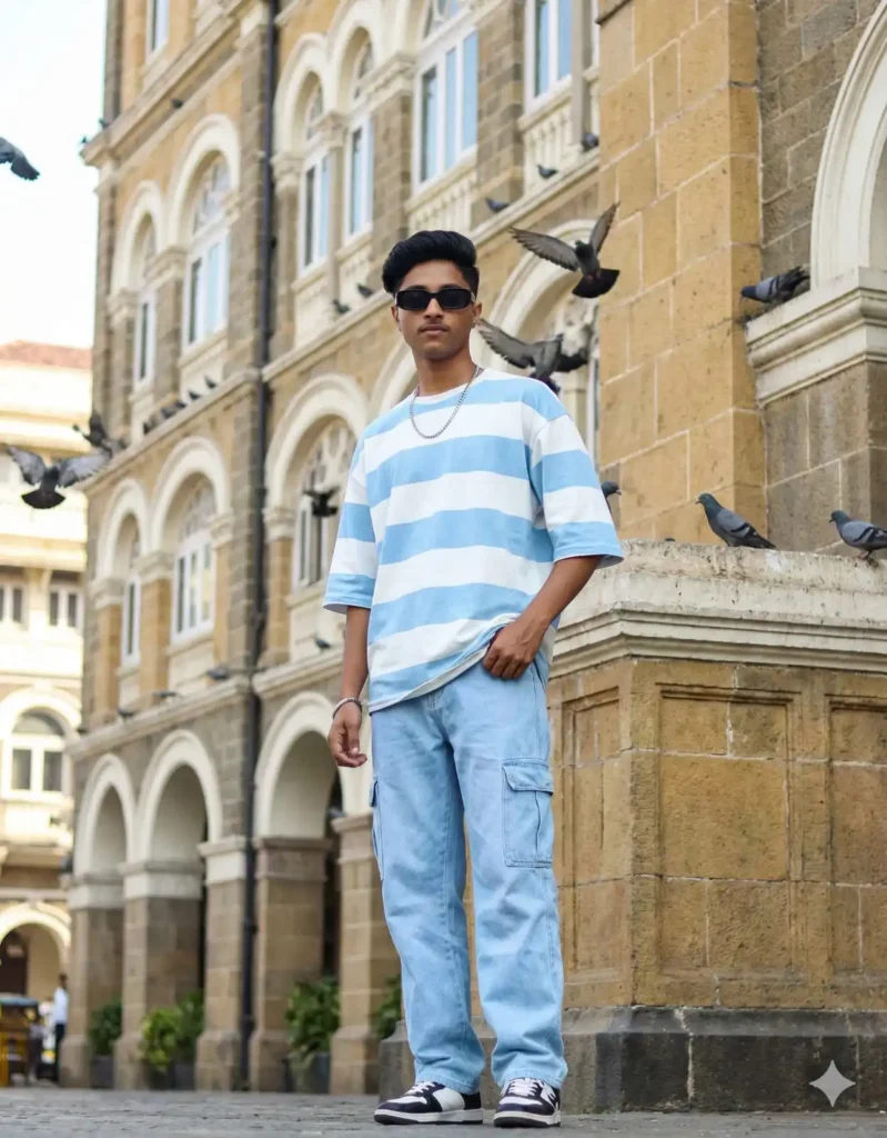 Young boy posing in a blue striped oversized T-shirt and cargo jeans at Grand Hotel Mumbai with flying pigeons – styled for 5 Gemini AI Photo Editing Prompts for Boys 2025. Scipuz