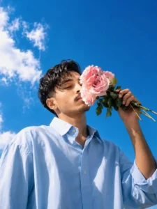 Young man holding pink flowers under a bright blue sky in aesthetic portrait photography style viral Instagram ai photo prompt